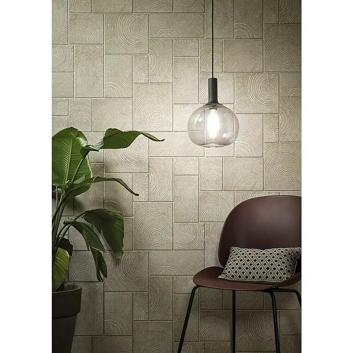 Marburg Natural Opulence Vliestapete - Beige, Holzoptik, 10,05 x 0,7 m - Stilvolle Innenaufnahme mit einer Wand aus dekorativen Holzimitatfliesen, einer Hängelampe, einer Pflanze und einem Stuhl mit Kissen.