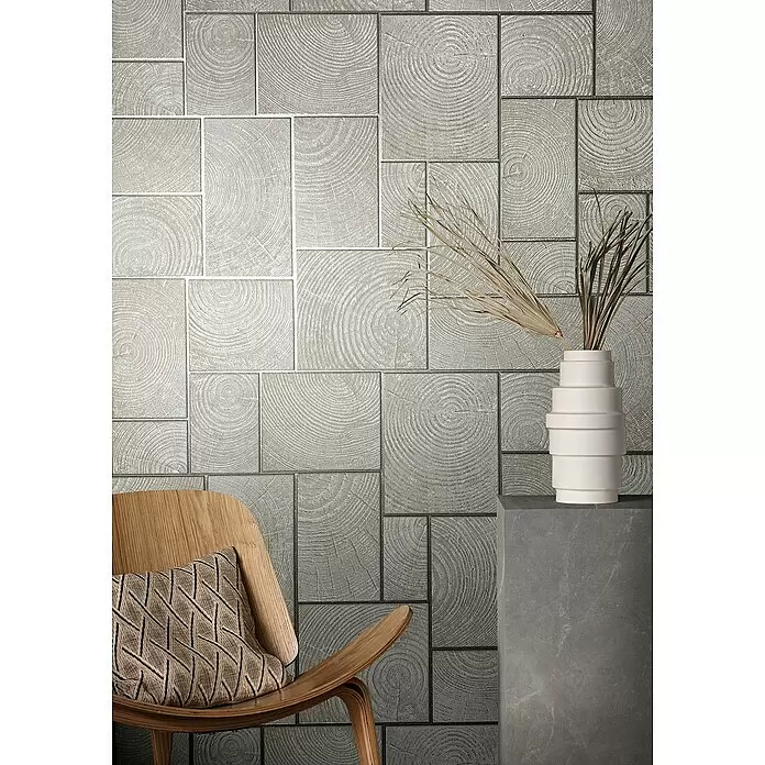 Marburg Natural Opulence Vliestapete - Beige, Holzoptik, 10,05 x 0,7 m - Helle graue Wandfliesen mit geprägtem Jahresringmuster, in einem Wohnraum mit Stuhl und Vase.