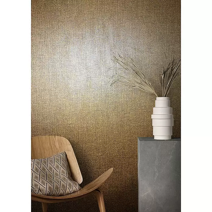 Marburg Natural Opulence Vliestapete - Kupfer, Uni, 10,05 x 0,7 m - Texturierte gold-beige Wandverkleidung mit sanftem Farbverlauf, präsentiert in einem modernen Raum mit Stuhl und Vase.