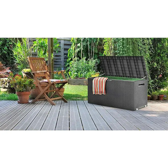 Jelenia Plast Garten-Aufbewahrungsbox Nizza - L x B x H: 120 x 52 x 60 cm, Polyrattan - Eine geflochtene, graue Gartenbox mit offenem Deckel steht auf einer Terrasse, daneben ein Holzstuhl und Pflanzen.
