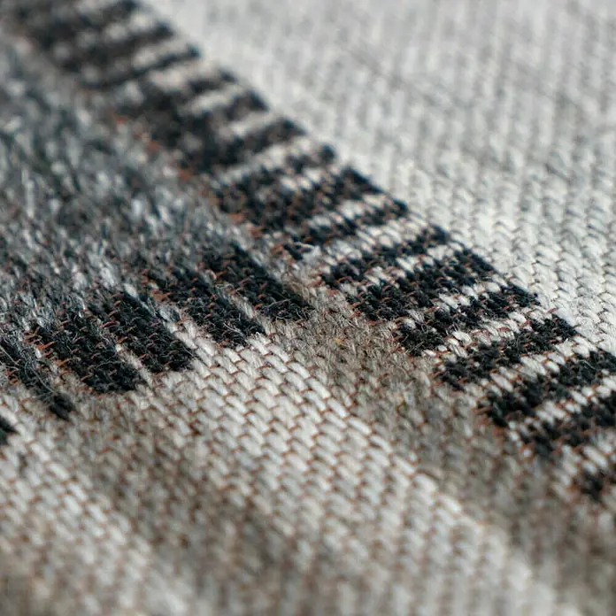 Kayoom Flachgewebeteppich Phönix - Grau/Braun, 230 x 160 cm, 75 % Wolle, 20 % Baumwolle, 5 % Polyester - Nahaufnahme eines Stoffes mit einem schwarz-grauen Muster, das die Textur und die Details des gewebten Materials hervorhebt.