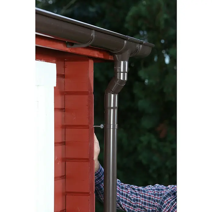 FunkeGruppe Dachrinnenhalter Vario - Nennweite: 70 mm, Braun, Kunststoff - Nahaufnahme eines installierten, braunen Dachrinnensystems an einer roten Hauswand, das Regenwasser ableitet.