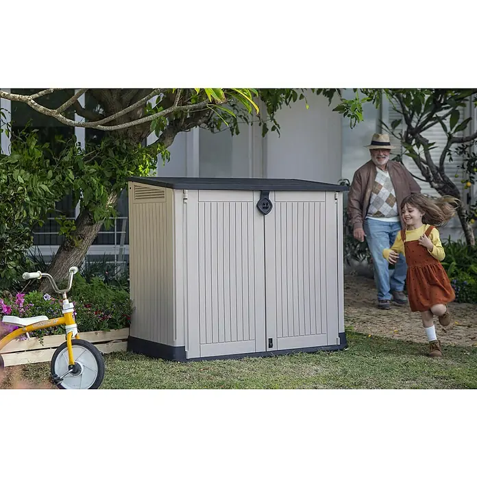 Keter Arcón Store It Out Midi - L x An x Al: 71,5 x 132 x 113,5 cm, Beige/Marrón, Plástico - Un cobertizo de jardín espacioso con puertas dobles para guardar herramientas, con un niño jugando y un anciano cerca.