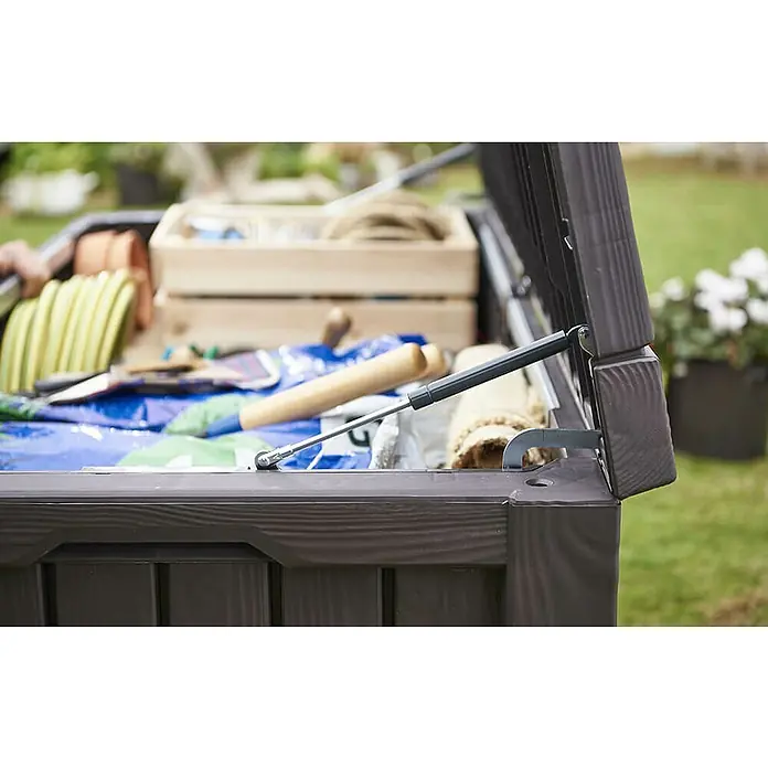 Keter Baúl para jardín Rockwood - 72,4 x 155 x 64,4 cm, 570 l - Vista de una caja de jardín marrón abierta, que muestra herramientas y equipos de jardinería en su interior, perfecta para soluciones de almacenamiento.