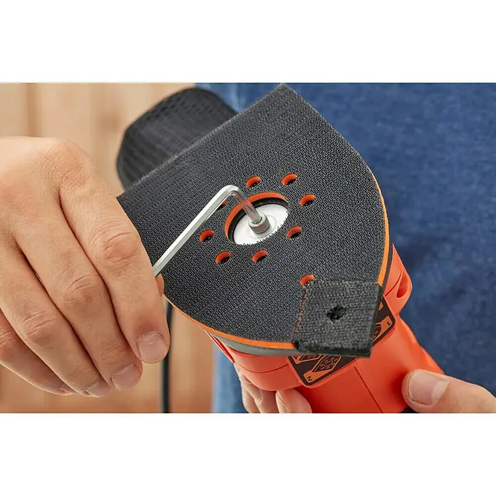 Black+Decker Lijadora multifunción eléctrica  BEW200-QS - 200 W, Número de oscilaciones marcha en vacío: 12.000 r.p.m., Diámetro circuito oscilante: 2 mm - Primer plano de una lijadora multifunción Black+Decker con una persona usando una llave Allen para cambiar la almohadilla de lijado.
