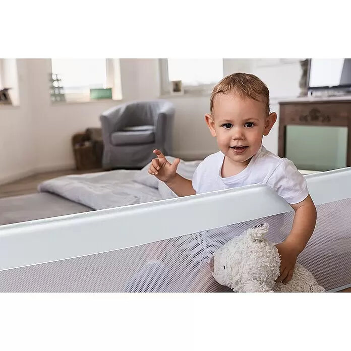 Abus Bettgitter Eric - Länge: 150 cm - Weißes Bettgitter mit Netzstoff, das ein lächelndes Baby sicher im Bett mit einem Teddybären hält.