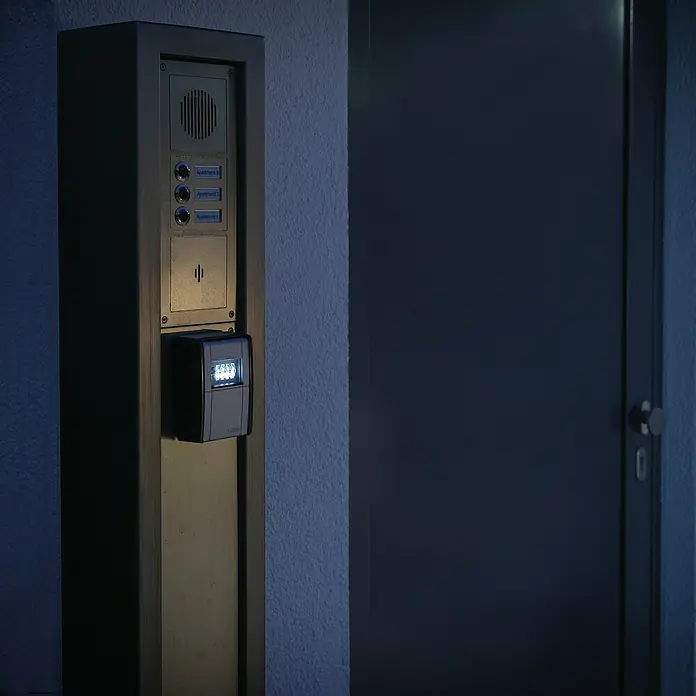 Abus Schlüsselbox Key Garage 787 LED - Geeignet für: Bis zu 20 Schlüssel, L x B x H: 45 x 80 x 120 mm, Mit LED-Beleuchtung - Nahaufnahme eines modernen Türkommunikationssystems mit Sprechanlage, Klingelknöpfen und beleuchteter Tastatur neben einer dunklen Tür.