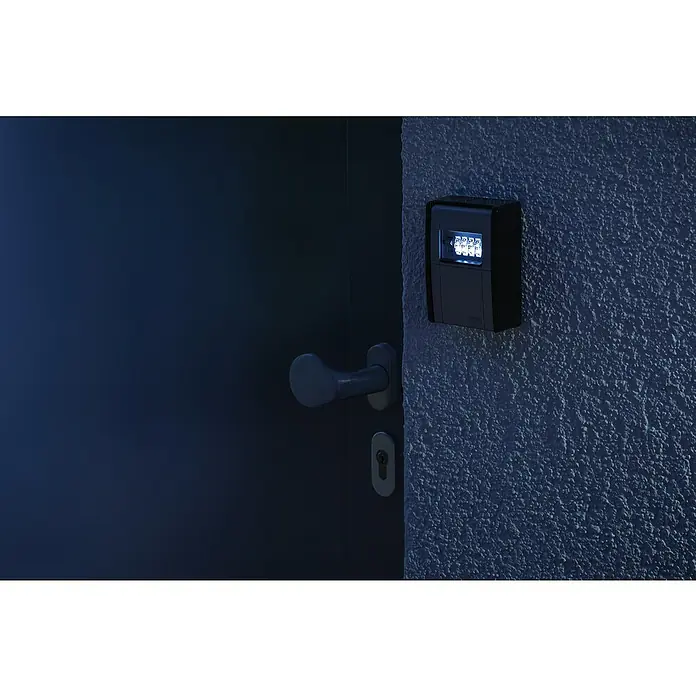 Abus Schlüsselbox Key Garage 787 LED - Geeignet für: Bis zu 20 Schlüssel, L x B x H: 45 x 80 x 120 mm, Mit LED-Beleuchtung - Nahaufnahme einer schwarzen Schlüsseltresor-Box mit LED-Beleuchtung an einer Wand neben einer Tür mit Griff und Schlüsselloch.