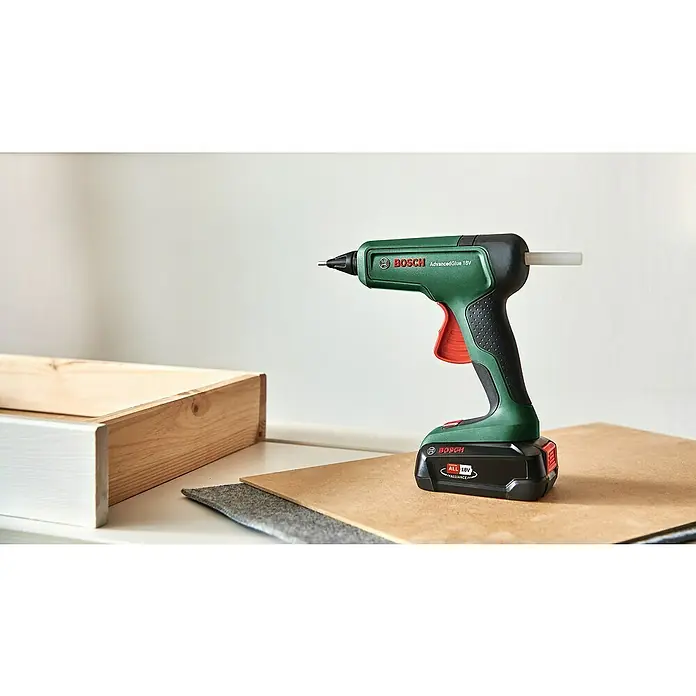 Bosch Power for All 18V Akku-Heißklebepistole AdvancedGlue 18V - 18 V, Ohne Akku, Temperaturbereich: 130 °C - 200 °C - Eine Bosch AdvancedGlue 18V Akku-Heißklebepistole, ideal für Hobbybastler und Handwerker, steht auf einem Tisch neben Holz und Filz.