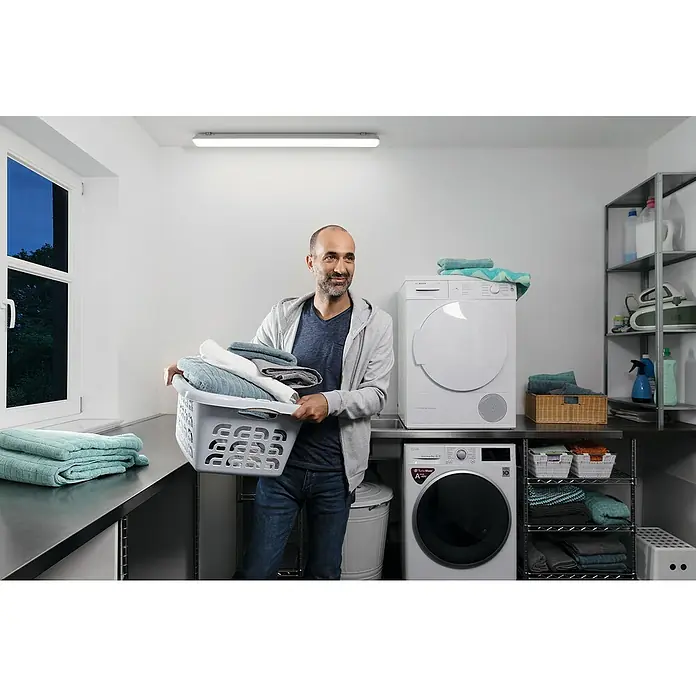 FeuchtraumleuchteLänge: 126,1 cm, IP65 - Ein Mann hält einen Wäschekorb in einem Waschraum mit Bosch-Waschmaschine und Trockner.