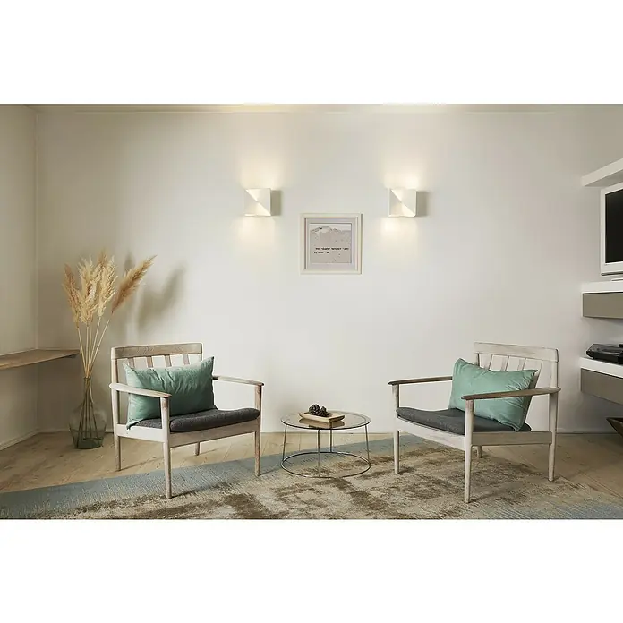Ledvance LED-Wandleuchte - 23 W, L x B x H: 30 x 15 x 10,5 cm, Weiß, Mehrfarbig - Wohnzimmer mit zwei Sesseln, einem Couchtisch und einer Wanddekoration, die eine gemütliche Atmosphäre schafft. Die Wandleuchten sorgen für ein warmes Licht.
