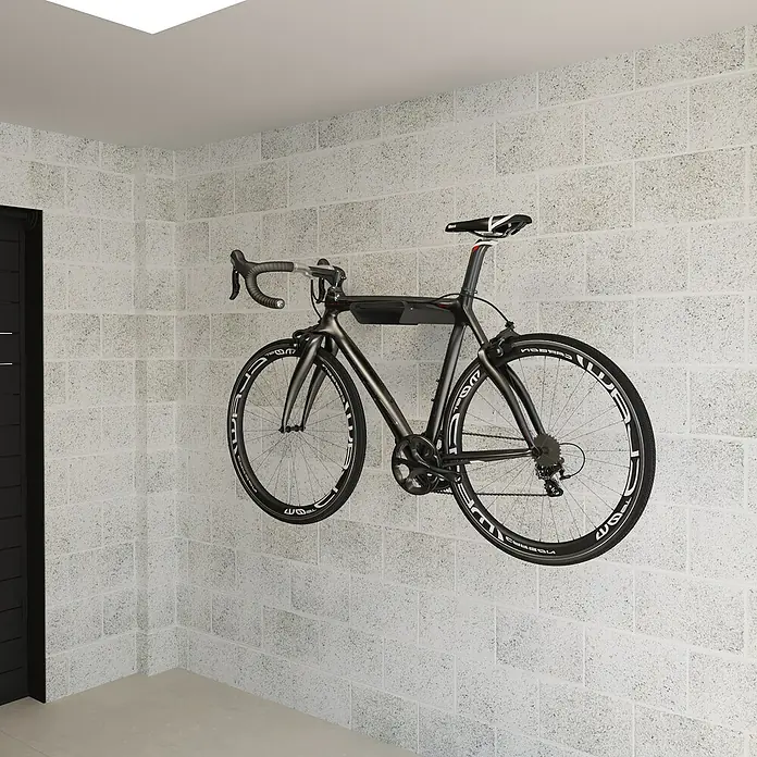 Rei Fahrradhalterung - L x B x H: 365 x 280 x 85 mm - Ein modernes Rennrad hängt an einer Wandhalterung in einem Raum mit weiß gestrichenen Ziegelwänden. Das Fahrrad ist schwarz mit weißen Akzenten.