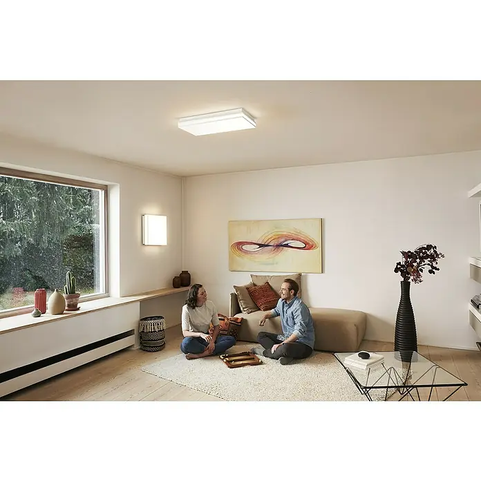 Ledvance LED-Deckenleuchte - 42 W, L x B x H: 60 x 30 x 8,6 cm, Weiß, Mehrfarbig - Das Bild zeigt eine moderne Deckenleuchte in einem hellen Wohnzimmer mit zwei Personen. Die Leuchte sorgt für eine angenehme Beleuchtung.