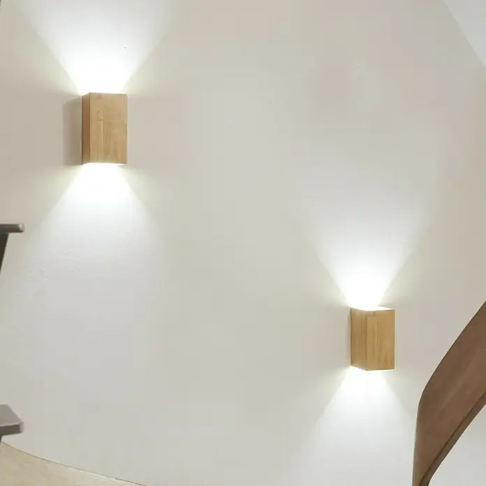 Ledvance Smart+ WiFi LED-Wandleuchte - 12 W, L x B x H: 11 x 11 x 21 cm, Gelb, Warmweiß - Zwei moderne Holzwandleuchten mit warmweißem Licht erhellen eine weiße Wand und sorgen für eine angenehme Atmosphäre im Raum.