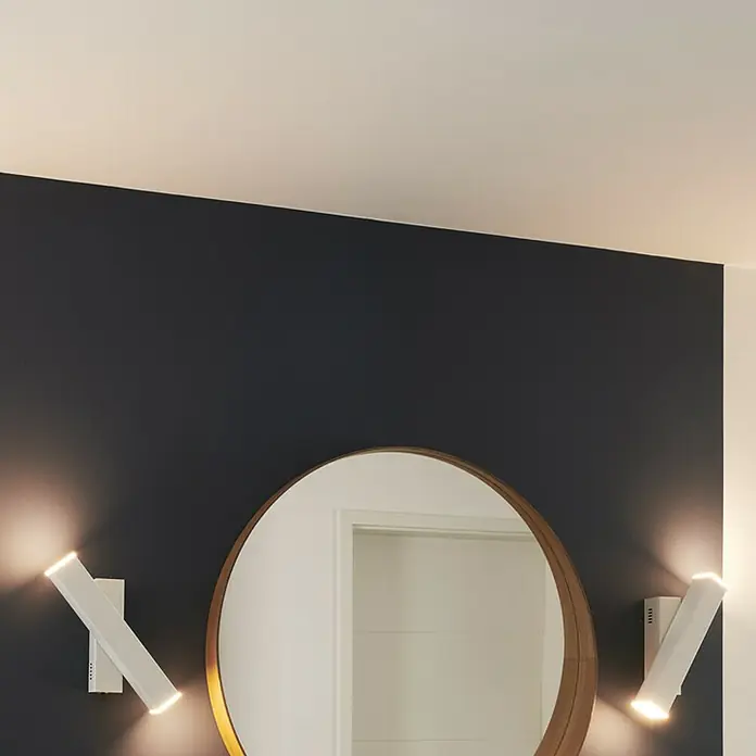 Ledvance LED-Wandleuchte - 12 W, L x B x H: 30,9 x 5 x 10,6 cm, Weiß, Mehrfarbig - Zwei moderne weiße Wandleuchten beleuchten einen runden Spiegel an einer dunklen Wand. Das Licht betont das minimalistische Design des Produkts.