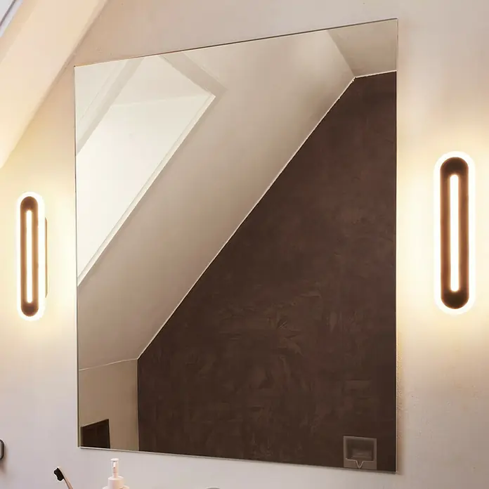 Ledvance Smart+ WiFi LED-Wandleuchte13 W, L x B x H: 30 x 7 x 5 cm, Schwarz, Warmweiß - Das Bild zeigt einen modernen Spiegel mit zwei vertikalen Leuchten an den Seiten, die ein warmes Licht ausstrahlen.