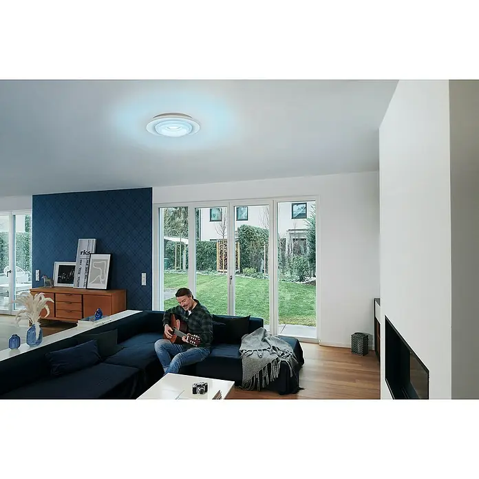 Ledvance LED-Deckenleuchte rund - 32 W, Ø x H: 50 x 10 cm, Weiß, RGBW - Ein modernes Wohnzimmer mit einem Mann, der Gitarre spielt, und einer stilvollen LED-Deckenleuchte mit bläulichem Licht.