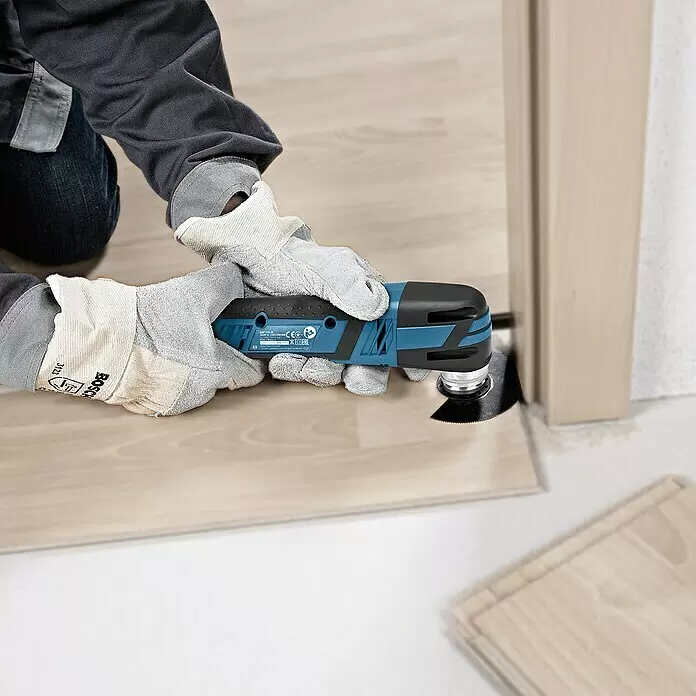 Bosch Professional Akku-Multifunktionswerkzeug GOP 12V-28 - 12 V, Ohne Akku, Mit L-Boxx - Eine Person mit Handschuhen verwendet ein blau-schwarzes Oszillationswerkzeug, um eine Holzdiele neben einem Türrahmen zu schneiden.