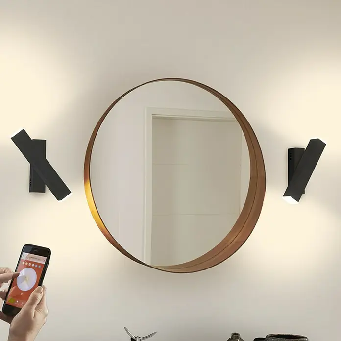 Ledvance LED-Wandleuchte - 12 W, L x B x H: 30,9 x 5 x 10,6 cm, Schwarz, Mehrfarbig - Wandmontierte Smart-LED-Leuchten mit Smartphone-Steuerung neben einem Spiegel, die modernes Design und Funktionalität vereinen.