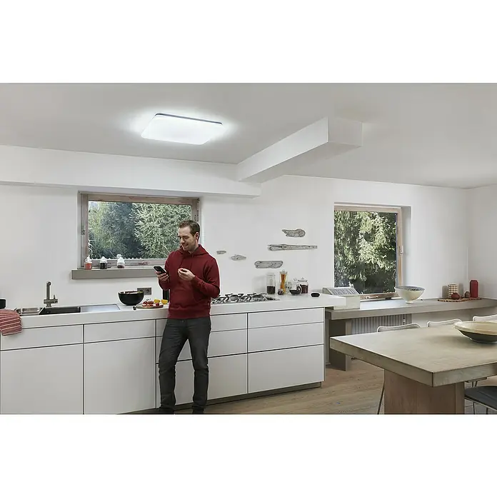 Ledvance LED-Deckenleuchte - 42 W, L x B x H: 53 x 53 x 8,5 cm, Weiß, Mehrfarbig - Ein Mann in einer modernen Küche mit einer hellen Deckenleuchte, die den Raum beleuchtet, während er sein Handy benutzt.