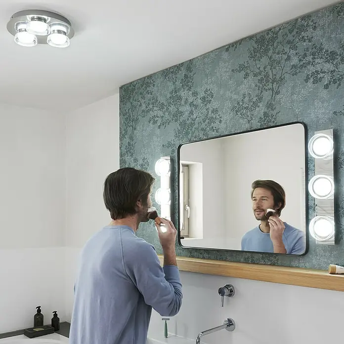 Ledvance LED-Wand- & Deckenstrahler - 18 W, L x B x H: 48 x 10 x 7,8 cm, Silber, Mehrfarbig, 1 Stk. - Ein Badezimmer mit einem Mann vor einem beleuchteten Spiegel, der sich rasiert. Die Spiegelleuchten sorgen für ideale Lichtverhältnisse.