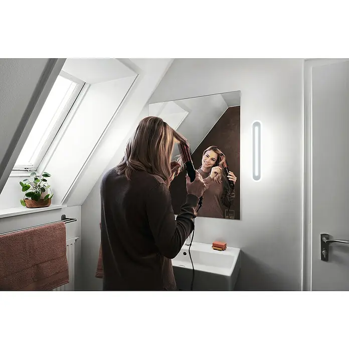 Ledvance Smart+ WiFi LED-Wandleuchte - 17 W, L x B x H: 40 x 7 x 5 cm, Weiß, Warmweiß - Eine Frau benutzt eine Philips StyleCare Iconic Styling Brush vor einem Spiegel, der das Lichtdesign des Badezimmers wiederspiegelt.