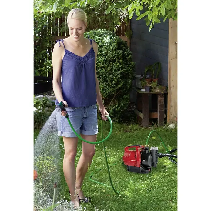 Einhell Hauswasserautomat GC-AW 6333 - 630 W, Max. Fördermenge: 3.300 l/h, Max. Druck: 3,6 bar - Eine Frau gießt mit einer roten Einhell Hauswasserwerk GE-WW 5537 E ihren Garten, um ihre Pflanzen mit Wasser zu versorgen.
