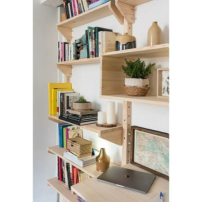 Astigarraga Wally Riel de fijación - L x An x Al: 96 x 4,5 x 4,5 cm, Madera maciza de pino - Primer plano de un sistema de estanterías de madera clara con libros, decoraciones y un portátil, que transmite un ambiente acogedor y organizado.