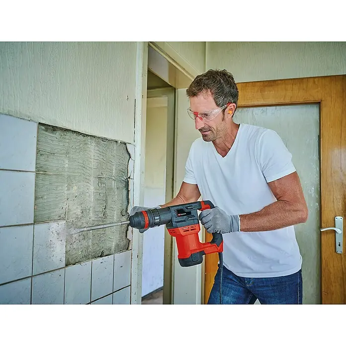 Einhell Martillo perforador TE-DH 5 - 750 W, 5 J, Alojamiento SDS-Plus - Hombre quitando azulejos con un martillo rotativo Einhell, usando gafas y tapones para una reforma segura y eficiente.