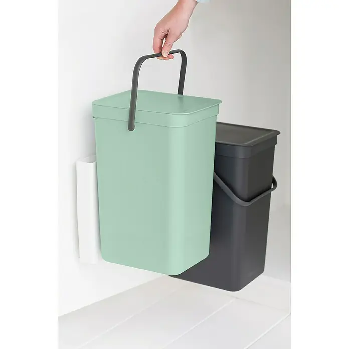 Brabantia Cubo de basura empotrado Sort & Go - 32 l, Plástico, Verde/Negro - Un cubo de basura verde menta Brabantia Sort & Go se sostiene en la mano, al lado de un cubo gris, perfecto para la separación de residuos en la cocina.