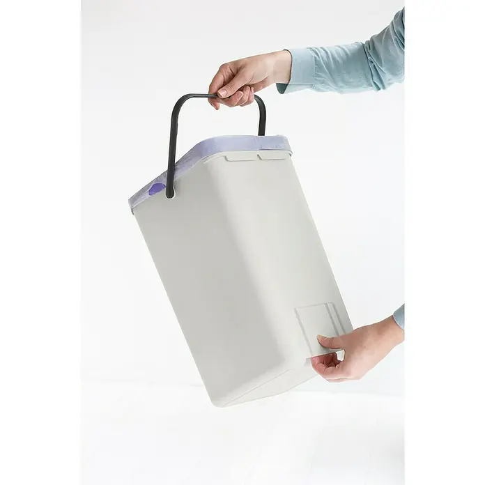 Brabantia Cubo de basura empotrado Sort & Go - 12 l, Blanco, Plástico - Una persona sostiene un contenedor de basura gris con tapa morada y asa negra, mientras abre un cajón.
