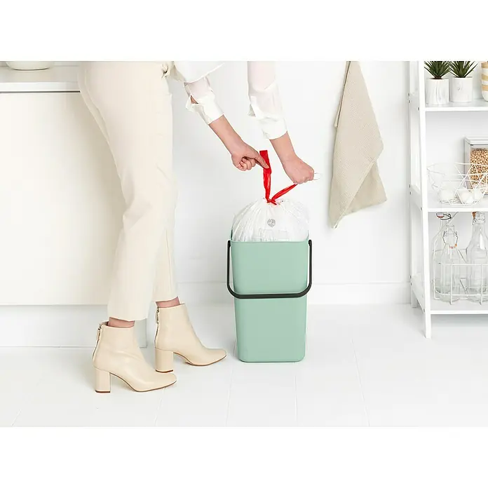 Brabantia Cubo de basura empotrado Sort & Go - 25 l, Verde, Plástico - Una persona está cambiando la bolsa de basura en un cubo de basura verde menta con un borde negro. La bolsa tiene un cierre rojo.