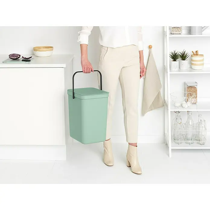 Brabantia Cubo de basura empotrado Sort & Go - 25 l, Verde, Plástico - Mujer sosteniendo un cubo de basura Brabantia Sort & Go verde menta con asa negra en una cocina moderna.