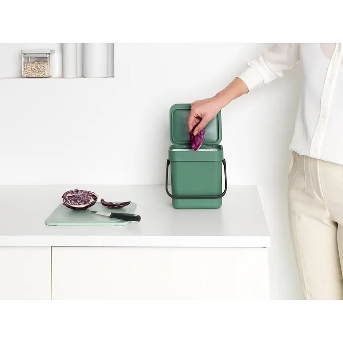 Brabantia Cubo de basura empotrado Sort & Go - 3 l, Plástico, Verde oscuro - Una persona tirando repollo en un contenedor de compostaje de cocina verde, que está sobre una encimera blanca.