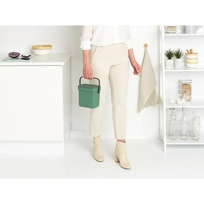 Brabantia Cubo de basura empotrado Sort & Go - 3 l, Plástico, Verde oscuro - Una mujer sostiene un cubo de compostaje verde en una cocina moderna. Perfecto para restos de cocina, con asa de transporte práctica.