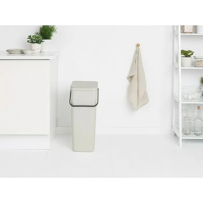 Brabantia Cubo de basura empotrado Sort & Go - 40 l, Blanco, Plástico - Un elegante cubo de basura gris con asa negra se sitúa en una cocina luminosa junto a un armario blanco.