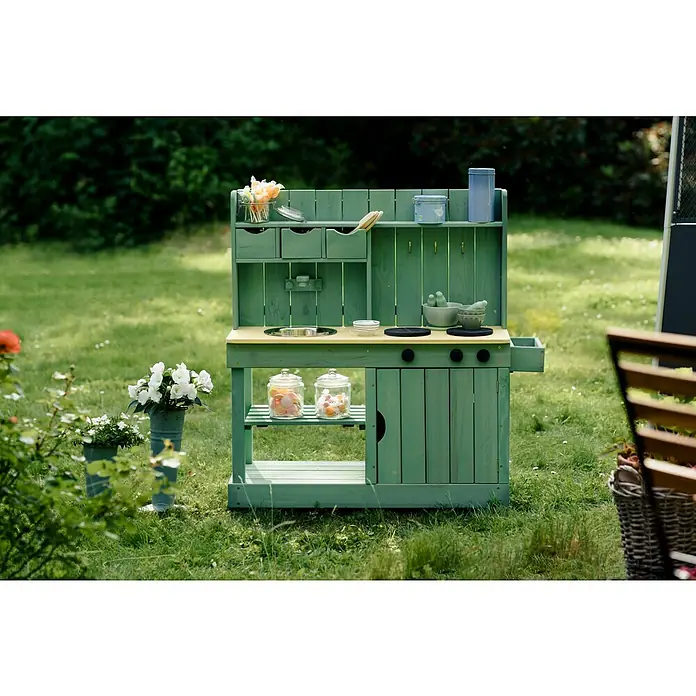 Muddy Buddy Matschküche Explorer - 102 x 40 x 105 cm, Holz, Salbeigrün - Eine grüne Spielküche mit gelber Arbeitsplatte und verschiedenen Utensilien steht auf einer Rasenfläche.