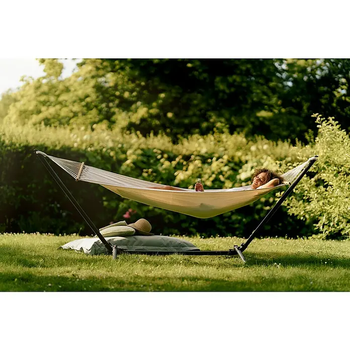 Hängematten-Set mit Gestell - L x B x H: 300 x 105 x 120 cm, Beige - Frau entspannt in einer Hängematte im Freien. Die freistehende Hängematte bietet einen bequemen und stilvollen Platz zum Entspannen im Garten.
