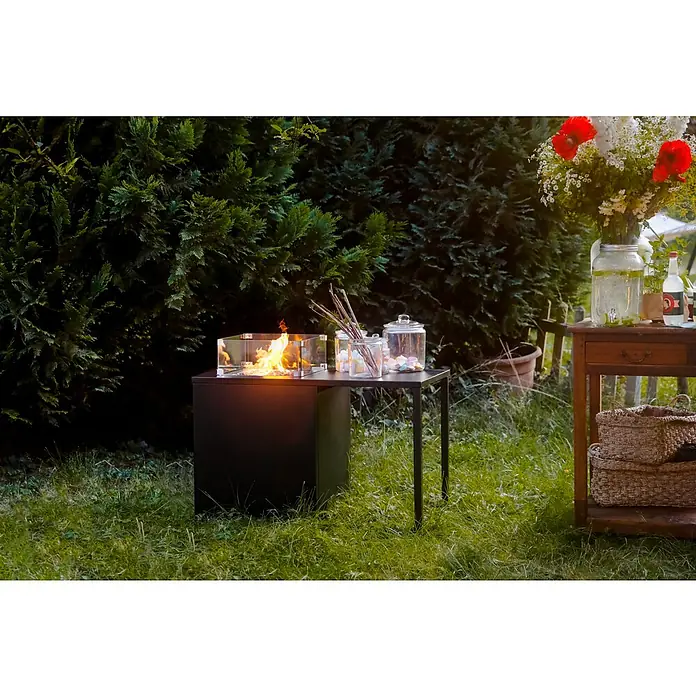 MWH Feuerstelle Palermo - 55 x 100 x 79 cm, Aluminium, Schwarz - Ein stilvoller Tischkamin mit Glasumrandung steht auf einem schwarzen Tisch, umgeben von Marshmallows und Zweigen.