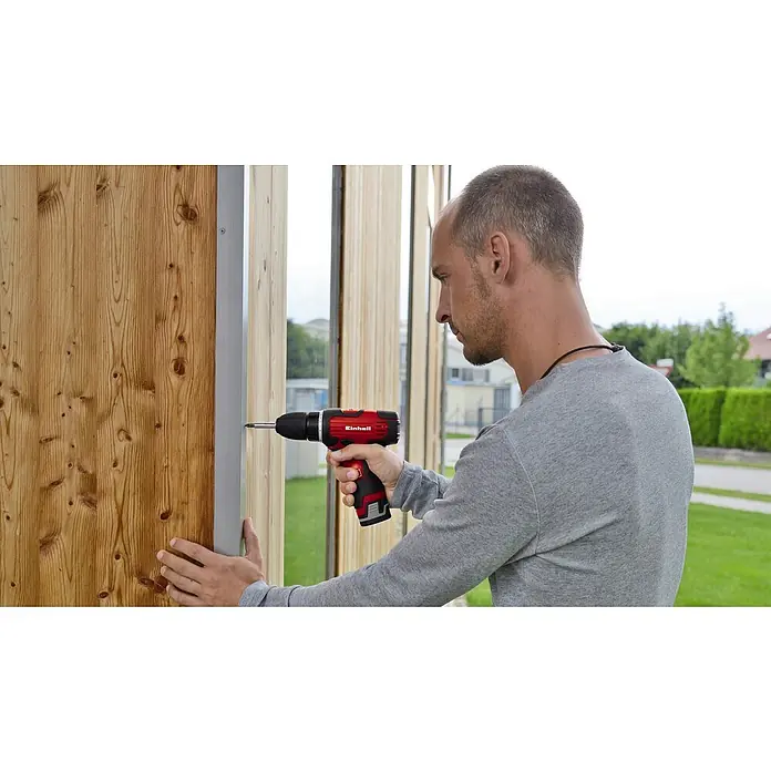 Einhell Akku-Bohrschrauber TH-CD 12-2 Li - 12 V, 1 Akku, 1,3 Ah - Ein Mann befestigt mit einem roten Einhell Akku-Bohrschrauber ein Holzbrett an einer Wand. Das Werkzeug ist gut sichtbar.