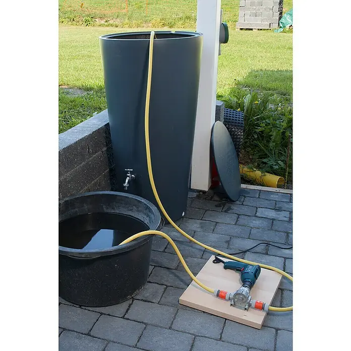 Wolfcraft Pumpe - 3.000 l/h, Förderhöhe: 24 m - 30 m, Metall - Eine Regentonne ist mit einem Schlauch an eine Pumpe angeschlossen, die von einem Bohrer angetrieben wird, um Wasser in einen Eimer zu befördern.