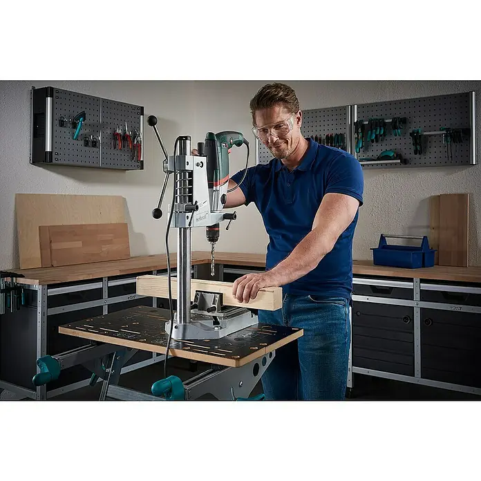 Wolfcraft Soporte de taladro - L x An x Al: 307 x 203 x 570 mm, Apertura máxima: 60 mm - Hombre operando un taladro de columna Wolfcraft con una pieza de madera sujeta. Ideal para perforaciones precisas en talleres.