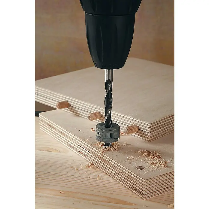 Wolfcraft Tiefenstopp-Set - 4 -tlg. - Ein Bohrer mit Tiefenanschlag bohrt Löcher in ein Holzbrett. Holzspäne liegen um das Bohrloch herum und auf der Oberfläche des Brettes.