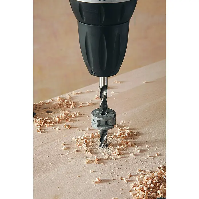 Wolfcraft Tiefenstopp-Set - 4 -tlg. - Nahaufnahme einer Bohrmaschine mit Tiefenanschlag beim Bohren in Holz, umgeben von Holzspänen.