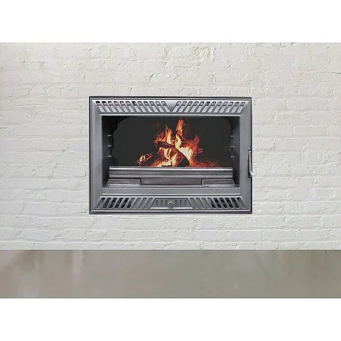 Insert Inuk Iron ventilado 70 - L x An x Al: 44,5 x 69,5 x 52 cm, 8 kW, 150 m³, Antracita - Primer plano de una chimenea con marco de metal gris y fuego crepitante en el interior, empotrada en una pared de ladrillo blanco.