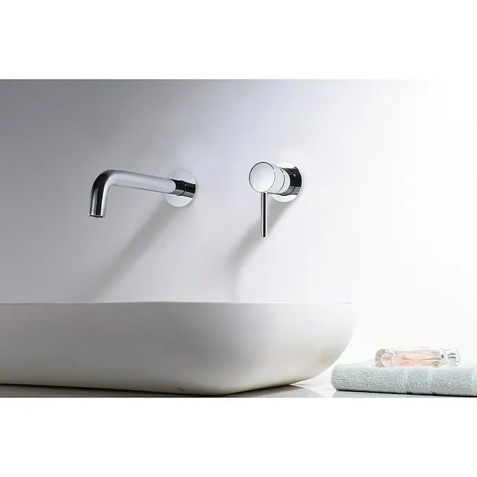 Imex Grifo de lavabo Etna - Cromo - Primer plano de un grifo moderno de pared sobre un lavabo blanco con una toalla y un frasco de perfume.