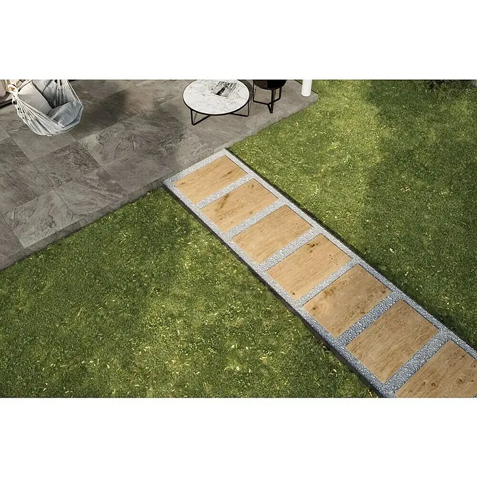 Atlas Concorde Solution Terrassenfliese Kortex Golden45 x 90 x 2 cm, Hellbraun, Matt - Bild einer eleganten Gartengestaltung mit einem stilvollen Holzweg, umgeben von grauem Kies und üppigem Grün. Die Terrasse ist mit grauen Fliesen ausgelegt.