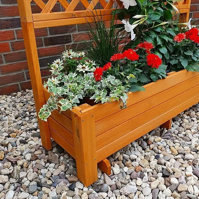 Promadino Pflanzkasten Romantica - Außenmaß (L x B x H): 120 x 38 x 140 cm, Holz, Honigbraun - Hellbrauner Blumenkasten aus Holz mit Spalier, gefüllt mit roten und weißen Blumen und Grünpflanzen, auf Kieselsteinen.