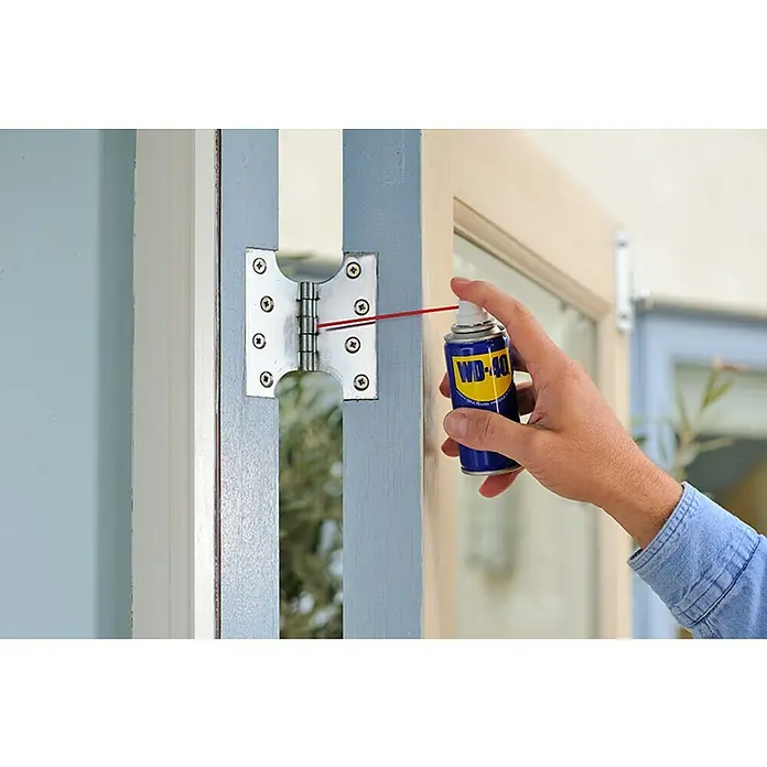 WD-40 Aceite para herrajes multiuso - 100 ml - Se está rociando WD-40 en una bisagra de puerta para lubricarla. WD-40 es un lubricante multiuso para uso doméstico e industrial.