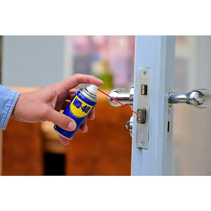 WD-40 Aceite para herrajes multiuso - 100 ml - Una mano rociando WD-40 Producto multiuso en una cerradura para lubricarla y mejorar su función.